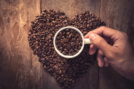 Man hand holding coffee cup and coffee bean on wooden table, Vintage colorの写真素材