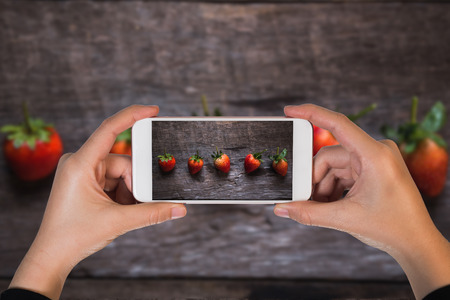 hand girl hoding mobile take photo of fresh strawberry on wooden background. Top view, flat layの写真素材
