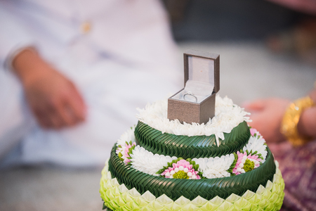 A diamond wedding ring in an open box on traditional Thai style garlandの写真素材