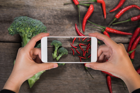 mobile take photo over fresh broccoli and chilli on wood table background. top viewの写真素材
