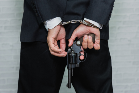 Arrested businessman in handcuffs and hold gun with hands behind backの写真素材