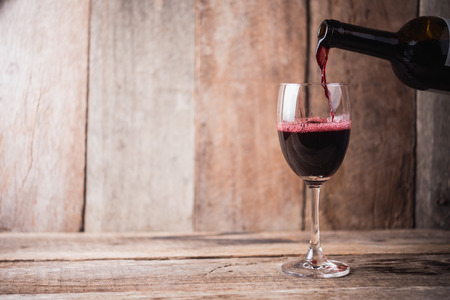 pouring wine into glass on wood backgroundの写真素材