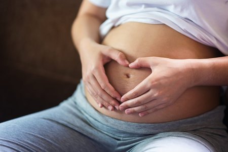 pregnant woman holding her hands on her swollen belly shaping a heart