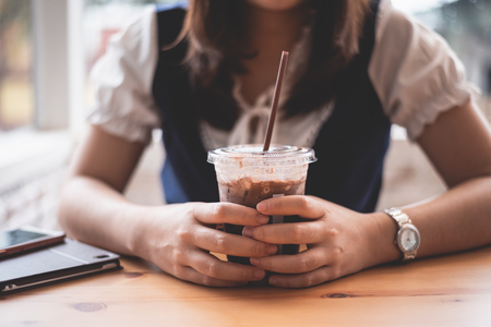 beautiful girl holding a cup of ice coffee in the cafeの写真素材