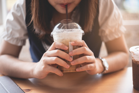 beautiful girl holding a cup of ice coffee in the cafeの写真素材