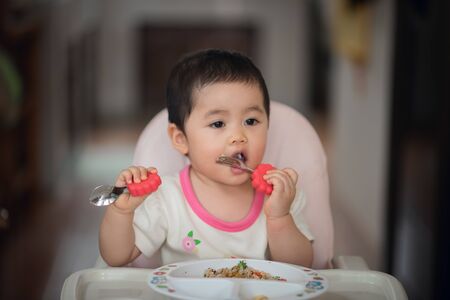 cute baby try to eating by herself on the baby seatの写真素材