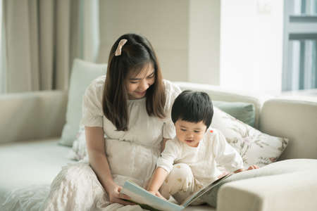 mother and daughter reading a book in the living roomの写真素材