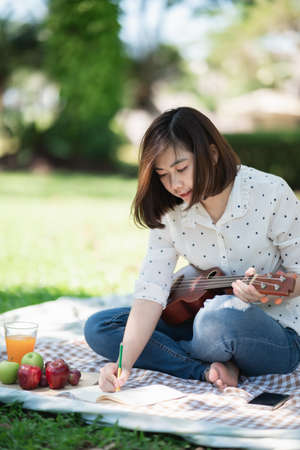 asian women sitting on the grass during a picnic and writing song in a parkの写真素材