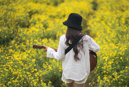 Asian young woman playing guitar and sing music in the park, asian woman palying guitar at yellow flowers gardenの写真素材