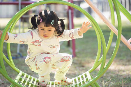Cute asian girl play on school or kindergarten yard or playground. Healthy summer activity for children. Little asian girl climbing outdoors at playground. Child playing on outdoor playground.の写真素材