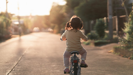 Asian toddler girl child learning to ride bicycle in sunny summer day, kid cycling at park, baby sport conceptの写真素材