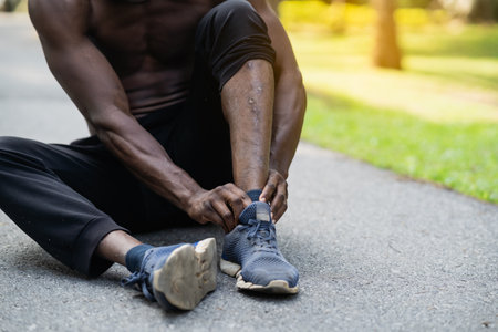 African runner man sitting on jogging track and feeling pain in his leg, copy space. Sports injury conceptの写真素材
