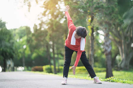 Senior asian woman body warming before exercising. Old woman stretching before jogging in garden, Sport athlete running concept.の写真素材