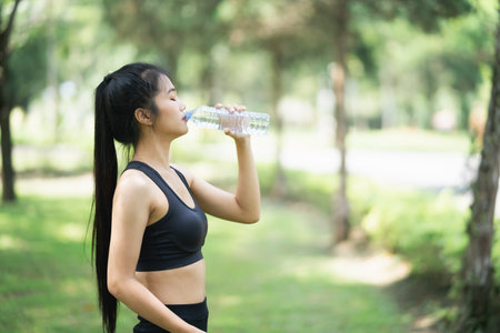 Sport women drinking water after running in the garden