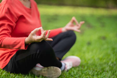 Senior asian woman practicing yoga lesson, breathing, meditating in garden. Half Lotus pose with mudra gesture, working out, Well being, wellness conceptの写真素材