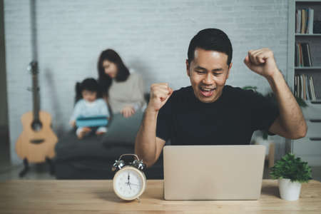 freelance man in eyewear working with laptop successful cheerful, sitting at wooden table. Pleasant happy man communicating in social network, family background.の写真素材