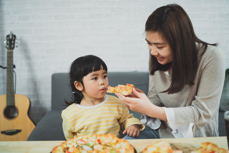 Asian mothers and children do activities at home. Mother is going to feed pizza for her kids....