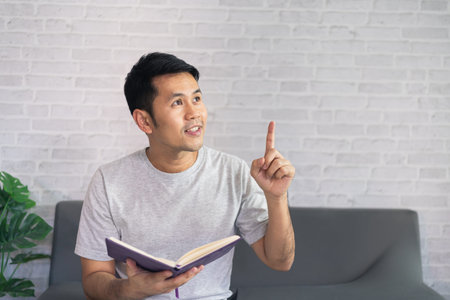 Smiling asian man wearing casual clothes sitting on a couch at the living room. Asian man using...