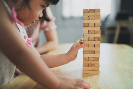 Asian daughter and mother smiling happily and laughing playing wooden toy tower sitting on sofa in living room at home, mother and daughter family activities playing happy gamesの写真素材