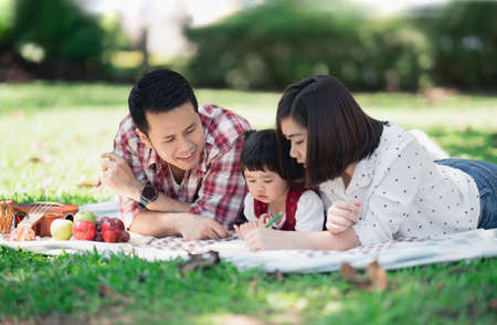 Family with children enjoying picnic in spring garden. Parents and kids having fun eating lunch outdoors in summer park. Mother and daughter playing ukulele in gardenの写真素材