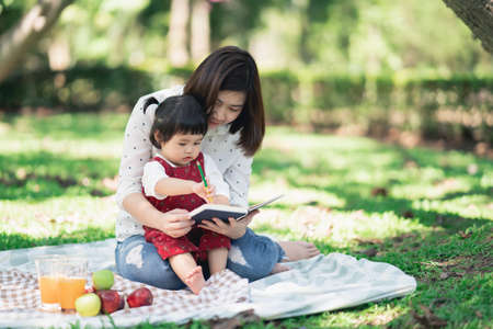 Family with children enjoying picnic in spring garden. Parents and kids having fun eating lunch outdoors in summer park. Mother and daughter painting in gardenの写真素材