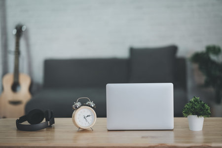 Close up view of worktable with laptop,  headphone, clock, acoustic guitar and decoration in home...