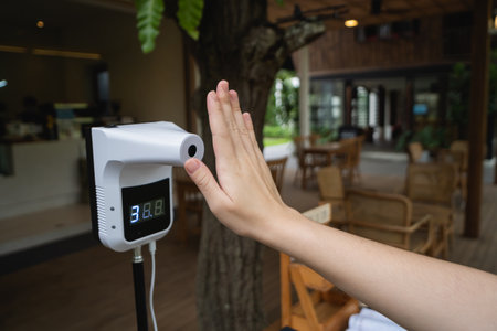 Digital thermometer for measuring body temperature by placing a hand over the sensor in a cafe checks of customers during the  pandemic.の写真素材