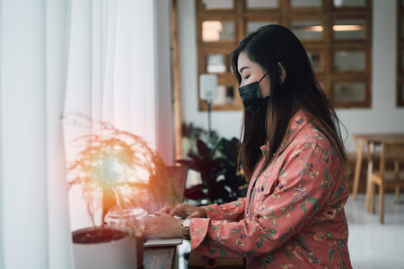 Asian young woman wearing mask working on laptop while sitting in cafe. young girl working with laptop.virus concept.の写真素材