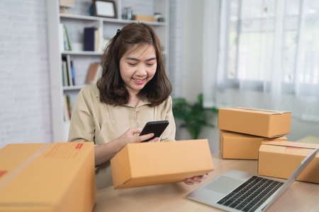 Asian delivery woman freelance smiling and working at home , checking list parcel boxes for sending or conveying parcels by mail.の写真素材