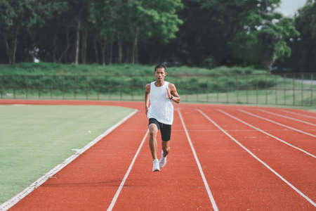 Athlete sportman runner training run on lane at the stadium in morning. Runner man wearing white vest to practice running prepare for competition race. Sport concept.の写真素材