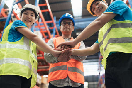 Group of industrial warehouse asian worker in safety suite hand stack celebrate successful or deal commitment. Logistics , supply chain and warehouse business.Teamwork unity under view concept.の写真素材