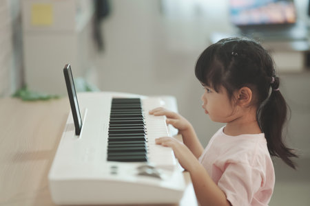 Asian cute girl learning online piano music with teacher by mobile phone or tablet. The idea of activities for the child at home during quarantine. Music learning study online concept.の写真素材