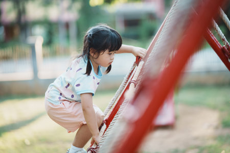 Cute asian girl smile play on school or kindergarten yard or playground. Healthy summer activity for children. Little asian girl climbing outdoors at playground. Child playing on outdoor playground.の写真素材