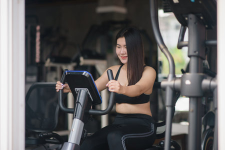 Asian woman exercising on a bicycle in the gym, smiling to lose weight, makes her healthy. exercise...