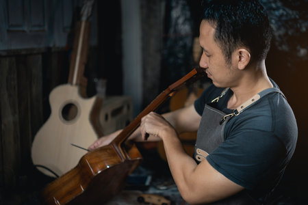 Guitar makers asian man making acoustic guitars in laboratory. Asian guitar maker builds high...