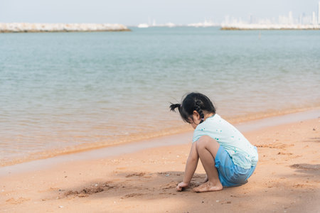 Asian cute little girl playing or making sand castle or digging with sand on tropical beach. Children with beautiful sea, sand and blue sky. Happy kids on vacations at seaside running on the beach.の写真素材