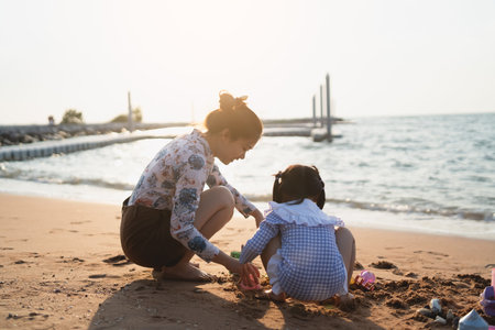Asian cute little girl and her mother playing or making sand castle or digging with sand on tropical beach. Children with beautiful sea, sand blue sky. Happy kids on vacations seaside on the beach.の写真素材