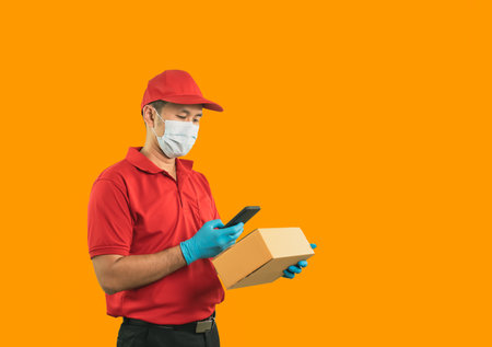 Crop picture of Asian delivery man worker wearing surgical mask and medical gloves in red uniform, hold parcel boxes for sending or conveying parcels by mail.の写真素材
