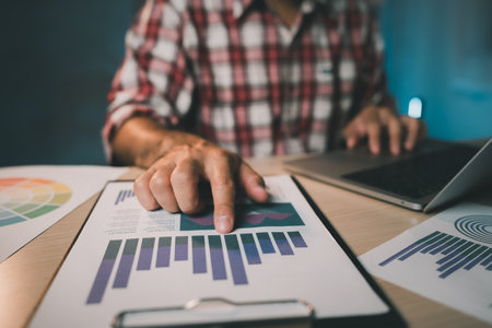 Freelance asian business man working with laptop and use hand to point the graph document. Man wearing plaid shirt red is rushing to work overtime for deadline. Business working concept.の写真素材