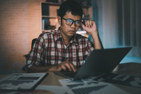 Asian freelance man having stressful depression sad time working on laptop home night. Depression man sad serios working from home. Man wearing plaid shirt red is rushing work overtime for deadline.の写真素材
