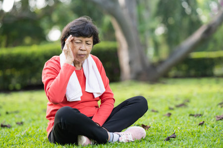 Senior asian woman hand holding head pain have a headache after running in park. Old asian woman resting at the park garden and holding painful headache or heat stroke symptoms. Sport health concept.の写真素材