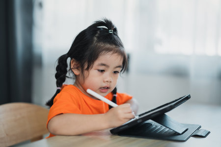Asian girl use digital pen and touch on screen tablet screen attentively. overstimulated children concept. Too much screen time. Cute girl watching videos while tv, Internet addiction concept.の写真素材