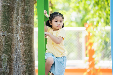 Cute asian girl smile climbing ladder and play on school or kindergarten yard or playground. Healthy summer activity for children. Little asian girl funny happy. Child playing on outdoor playground.の写真素材