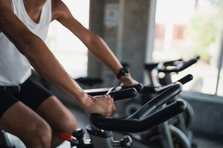 Close up hands of asian sportsman exercising on a bicycle in the gym, determination to cardio lose weight, makes her healthy. exercise bike man fitness sport concept.の写真素材