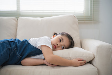 Cute little girl child sleeping on couch sofa with soft pillows at living room at home. Baby girl lying on the sofa couch bed.の写真素材