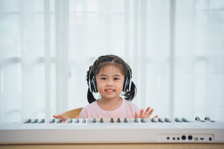 Asian cute girl smile and wearing white headphone playing learning online piano music in the living room at home. The idea of activities for the child at home during quarantine. Music learning study.の写真素材
