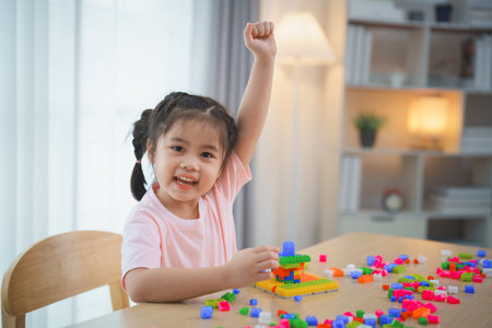 Joyful Asian girl happy and smiling raise her hand playing colorful Lego toys, sitting on the table in the living room, creatively playing with Lego, building colorful structures creativity imagine.の写真素材
