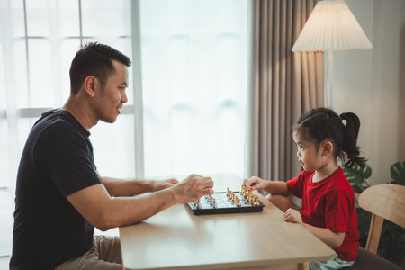Education studying concept. Little cute asian baby girl children playing chess with her father dad in the living room at home.Smart kid. Little genius Child. Intelligent game.Chessboard.の写真素材