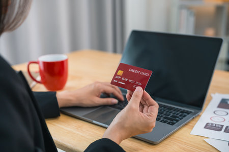 Back side. Businesswoman holding credit card and using laptop computer to shopping online. working at home. Online shopping, e-commerce, internet banking, spending money, shopping from anywhere.の写真素材
