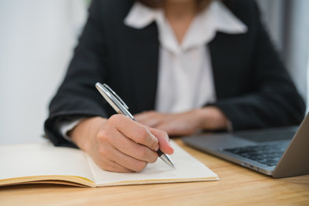 Close up of handAsian businesswoman wearing suit and writing notes book and working laptop on table at home. Entrepreneur woman working for business at living room home. Business work home concept.の写真素材